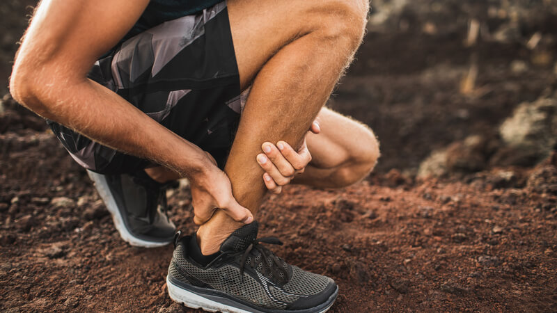 person kneeling down and holding their ankle