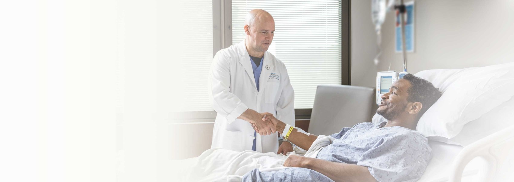 Doctor in white coat standing, holding hand of hospitalized male patient at Aiken Regional Medical Centers in Aiken South Carolina